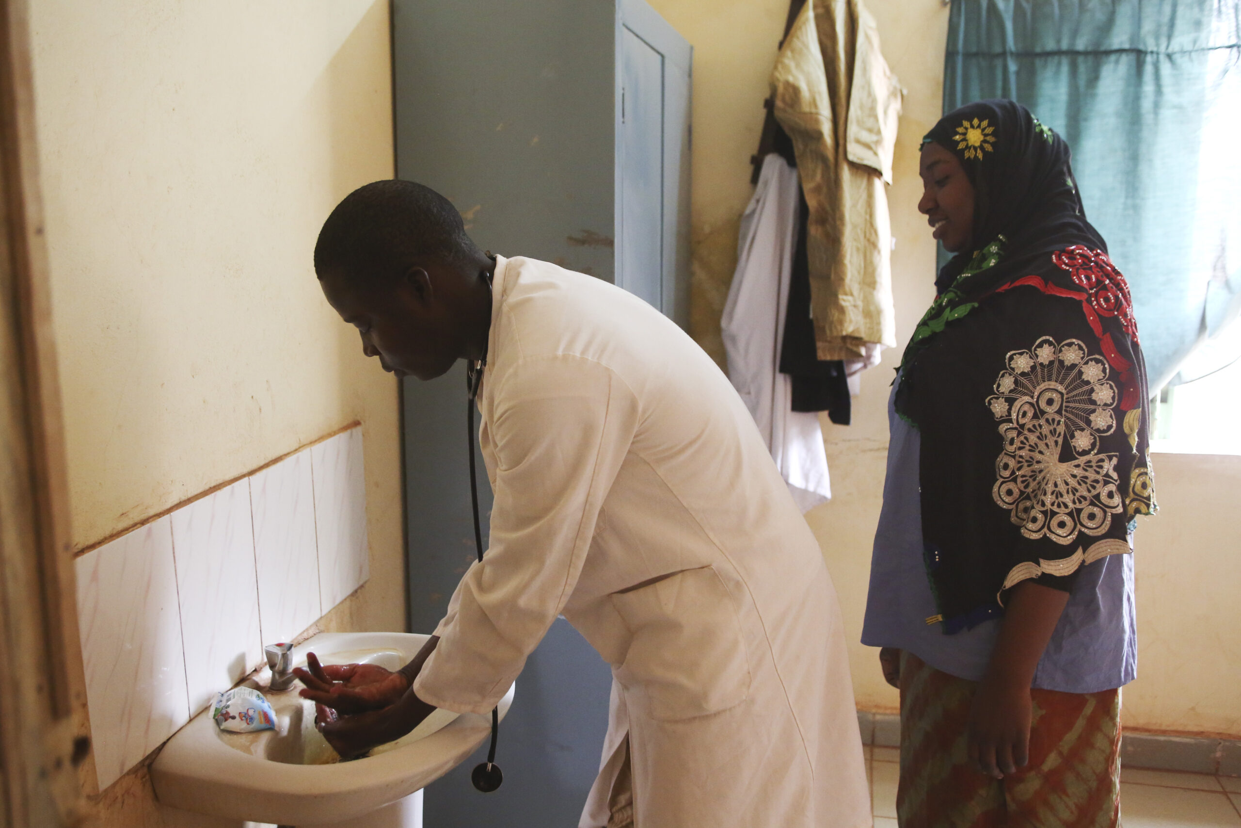 Doctor washes hands while nurse waits behind him to do the same.